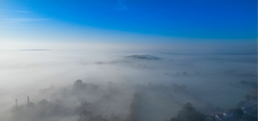 Aerial view of a small town shrouded in a misty fog, with white fluffy clouds surrounding it