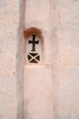 Fototapeta na wymiar Vertical shot of a window carved on a pink wall in the shape of a cross