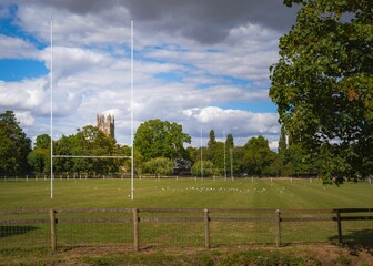 Rugby goal post in an open field surrounded by trees and a cloudy sky in the background