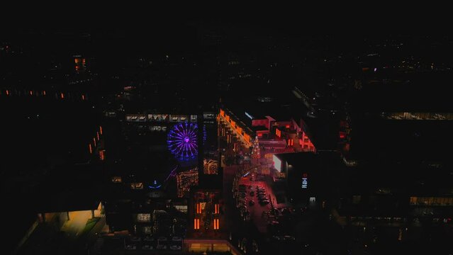 Drone footage over colorful Ferri Wheels and colorful city buildings at night