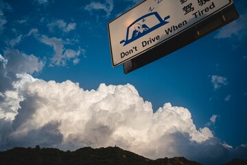 Warning sign reminding drivers to not drive when tired against a blue sky with a white fluffy cloud