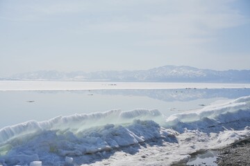 Scenic view of a frozen shore against a lake and a snowy mountain range in winter