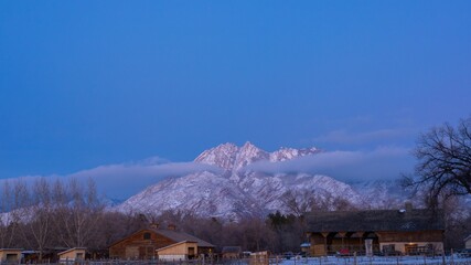 snow - covered mountains rise above some homes in a ranch