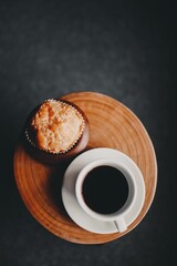Vertical shot of a cup of hot coffee and a sweet cookie on the wooden surface