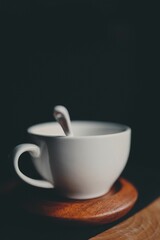 Vertical shot of a  white cup with a spoon on a wooden surface with a black background