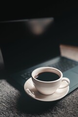 Closeup of a white a coffee cup  next to a laptop on a table