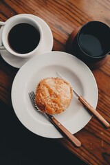Vertical shot of a cup of hot coffee and a sweet cookie on the wooden surface
