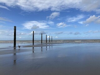 Beach with wooden posts extending out into the crystal blue waters against a cloudy blue sky