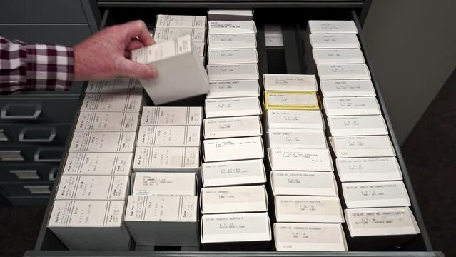 Library man organizing a microfiche inside an archive drawer and close it