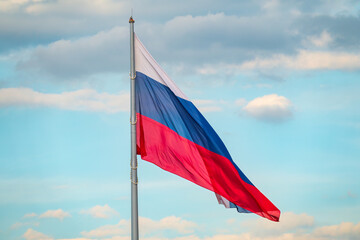 Russian tricolor flag waving in the wind against a blue sky.