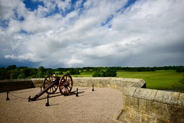 Fototapeta na wymiar a cannon stands against a wall overlooking a grassy field with clouds