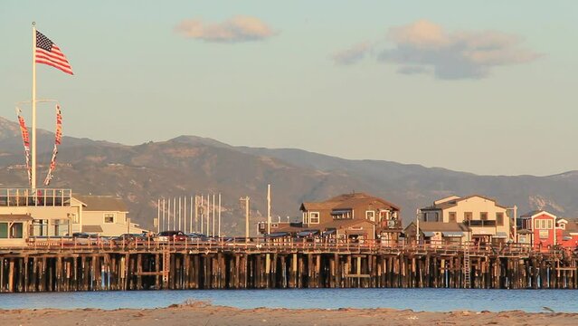 Stearns Wharf pier in Santa Barbara, California during sunset circa 2012. American flag waving and sea birds passing in the foreground.