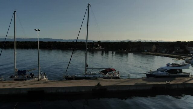 A circuling shot of a sailng boat docked on a stone pier. The sun is just rising so the water has a beautiful reflection and nice silky smooth waves.
