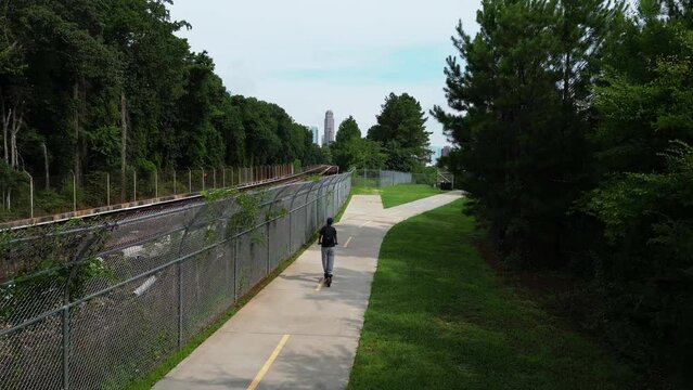 Back view of girl using electric scooter. Riding on path in park in city. Modern individual mobility solution. Atlanta, Georgia, USA