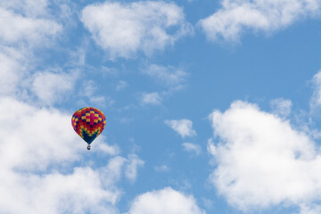 An isolated multicolored hot air balloon floats in the air with white clouds and a crisp blue sky.
