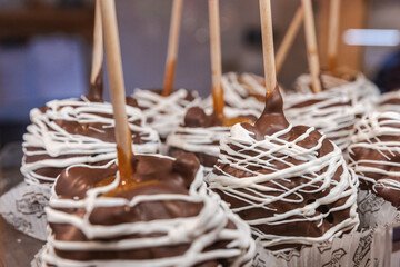 Several chocolate dipped caramel apples with a white chocolate drizzle arranged in a display at a market during the winter holidays.
