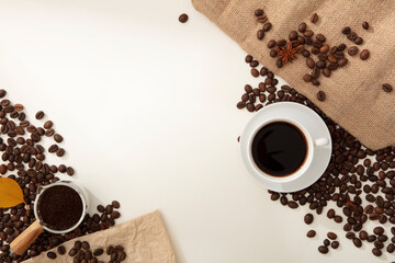 Lots of coffee beans displayed on white background with white cup of coffee and brown burlap. Top view and copy space. Coffee has become the spiritual drink of many Vietnamese.