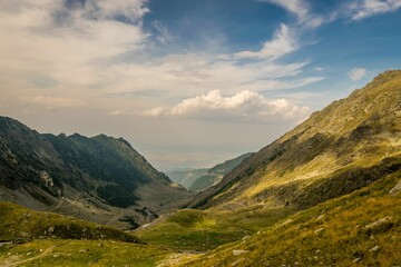 A vibrant green valley, lush rolling hills, and a bright blue sky with billowy white clouds.