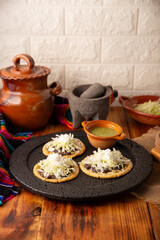 Sopes. Mexican typical food prepared with flattened fried corn dough covered with refried beans, green or red sauce, lettuce, cheese, onion and sour cream. Served on stone comal plate.