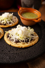 Sopes. Mexican typical food prepared with flattened fried corn dough covered with refried beans, green or red sauce, lettuce, cheese, onion and sour cream. Served on stone comal plate.