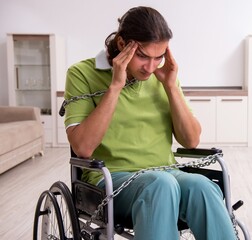 Young male invalid in wheel-chair suffering at home