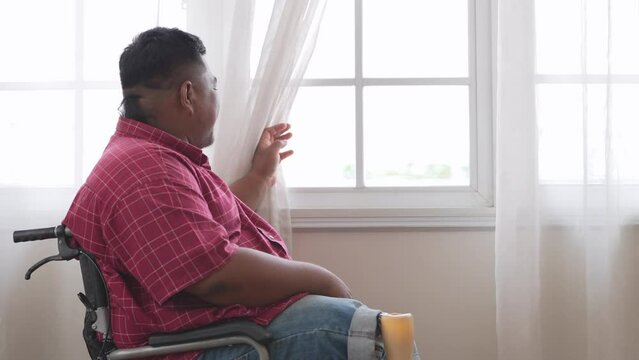 Asian man feeling uncomfortable in a Wheelchair at the living room. male setting and adjusting mechanic steel leg at home.