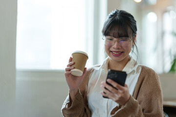Positive asian young female accountant using a smartphone at her office desk. Woman relaxing on her mobile application.