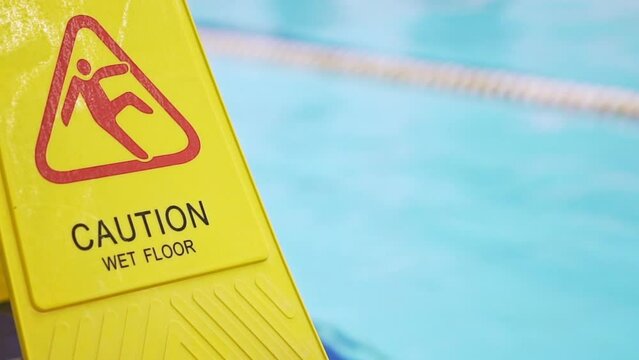 The inscription in English - carefully wet floor. Yellow plastic warning sign symbol, floor near the swimming pool is slippery. Safety rules in public places. Summer activity concept. Beware of danger