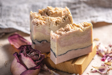 Delicate cute pieces of natural soap on a wooden soap dish on a background of fabric and pink flowers and petals nearby. Beautiful postcard
