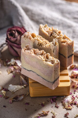 Delicate cute pieces of natural soap on a wooden soap dish on a background of fabric and pink flowers and petals nearby. Beautiful postcard
