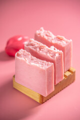 Cute pink pieces of handmade natural soap on a wooden soap dish on a pink background. Modern and safe cosmetic products for skin care and interesting hobby