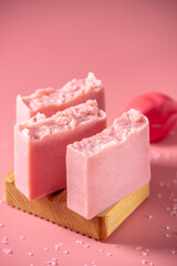 Cute pink pieces of organic eco soap on a soap dish made of natural wood on a pink background. Concept of modern and safe cosmetic products for skin care