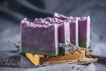 Pieces of natural lavender handmade soap on a wooden soap dish and on a dark fabric background with...