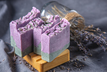 Pieces of natural lavender handmade soap on a wooden soap dish and on a dark fabric background with dry flowers. Concept of organic cosmetics, a useful and interesting hobby, a beautiful postcard