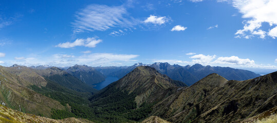 Summit of the Kepler track with a view of a lake in the middle of a mountain range during a sunny day, New Zealand