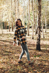 A beautiful girl in jeans and a plaid shirt walks in a birch grove. Portraits of a brunette girl in nature, in the autumn forest