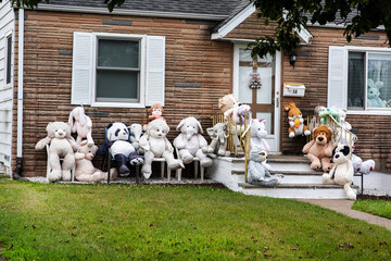 Teddy bears of different colors, shapes and sizes in front of an American house.