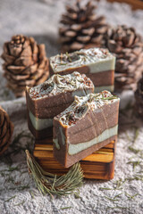 Fragrant pieces of natural coniferous soap handmade on a wooden soap dish, surrounded by cones and needles on a background of fabric. Atmospheric winter postcard