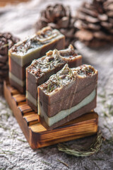 Fragrant pieces of natural coniferous soap handmade on a wooden soap dish, surrounded by cones and needles on a background of fabric. Atmospheric winter postcard