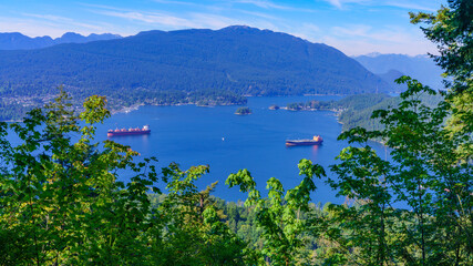 Fototapeta na wymiar Oil tankers on pristine waters of Burrard Inlet, backed by forested mountains.