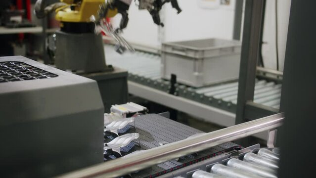 Medium shot of a yellow automatized robotic arm taking a metal car part from the conveyor belt and taking it to the next step in the production line factory