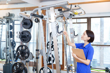 スポーツジムのトレーニングマシンを点検する女性スタッフ