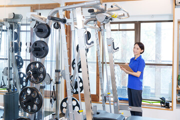 スポーツジムのトレーニングマシンを点検する女性スタッフ