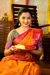 Vertical shot of happy indian girl holding flower plate for diwali celebration by looking at camera...