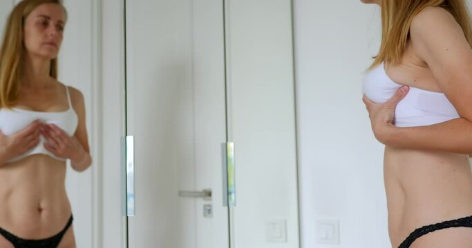 Woman staying in lingerie near mirror in bedroom and examines her breast