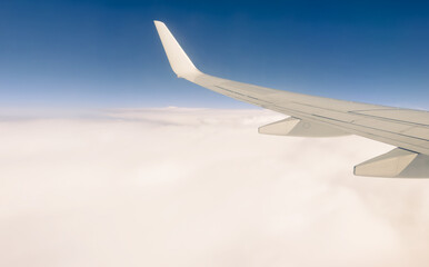 Obraz premium White wing from airplane window on sunny day. Great views of landscape. Aerial view of clouds through a plane window. Wing of airplane with blue sky and beauty clouds