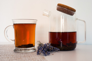 Black tea in a glass cup and glass teapot on a napkin and lavender on white table with white background