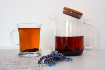 Blured black tea in a glass cup and glass teapot on a napkin and lavender on white table with white background