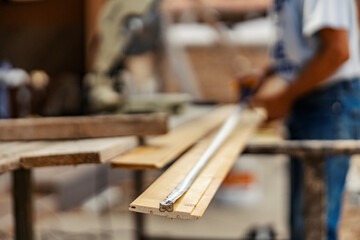 Selective focus on wooden board and construction meter with blurry worker on site.