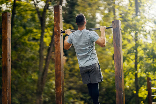 Rear view of a sportsman doing chin ups in outdoor nature gym.